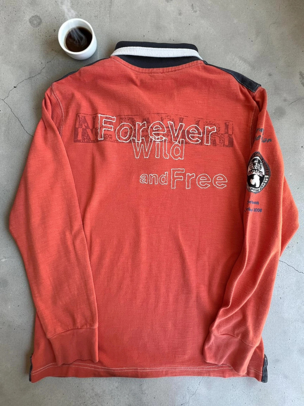 Napapijri orange long sleeve polo with embroidered patches and "Forever Wild and Free" graphic.