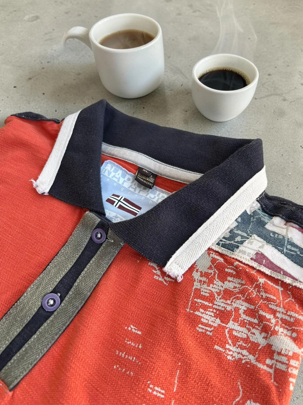 Napapijri orange long sleeve polo with embroidered patches and "Forever Wild and Free" graphic.