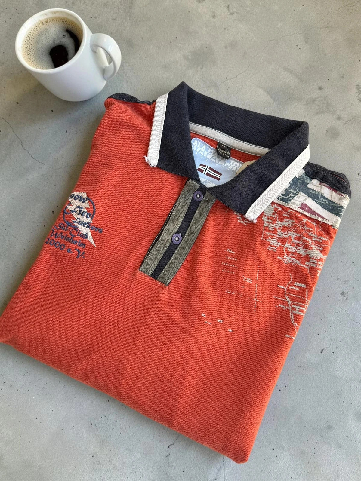 Napapijri orange long sleeve polo with embroidered patches and "Forever Wild and Free" graphic.