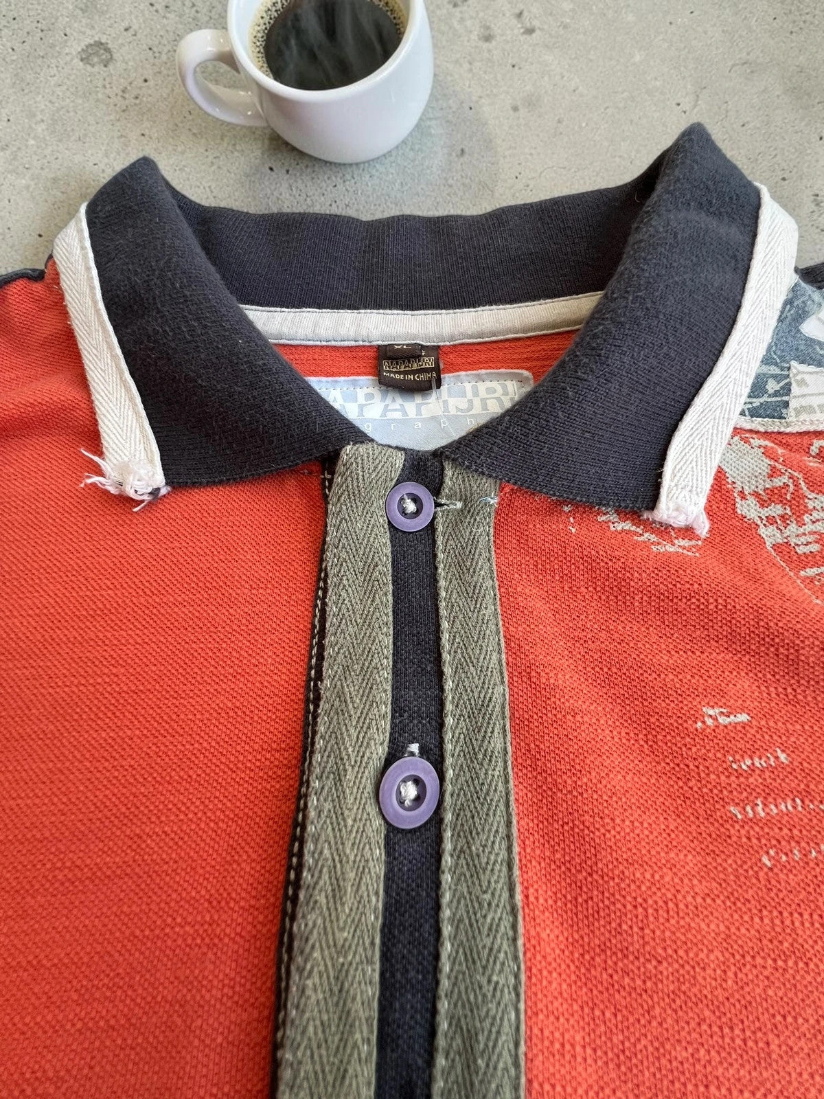 Napapijri orange long sleeve polo with embroidered patches and "Forever Wild and Free" graphic.